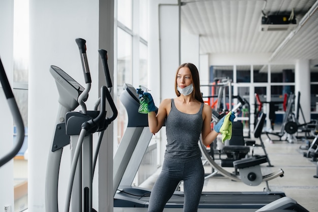 The girl in the mask disinfecting the gym equipment during a pandemic.