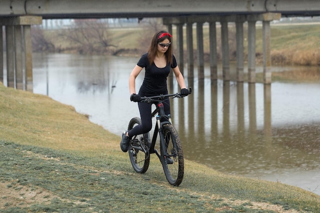 Girl on a mountain bike on offroad beautiful portrait of a cyclist in rainy weather Fitness girl rides a modern carbon fiber mountain bike in sportswear Closeup portrait of a girl in red bandana