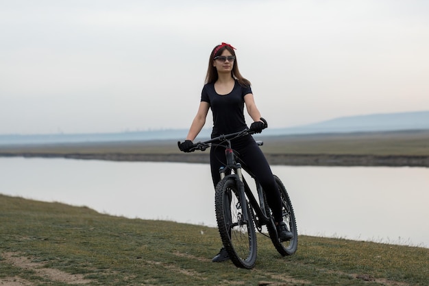 Girl on a mountain bike on offroad beautiful portrait of a cyclist at sunset Fitness girl rides a modern carbon fiber mountain bike in sportswear Closeup portrait of a girl in a helmet and glasses