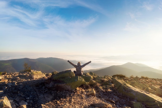 Girl on mountain top looking at beautiful mountain valley in fog at sunset