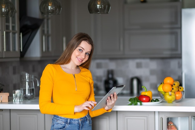 A girl in an orange sweater holds a tablet in search of a recipe