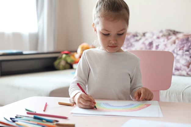 Girl painting rainbow at home, a symbol of UK National Health Service (NHS). Thanks to the doctors for their work. Stay at home Social media campaign.