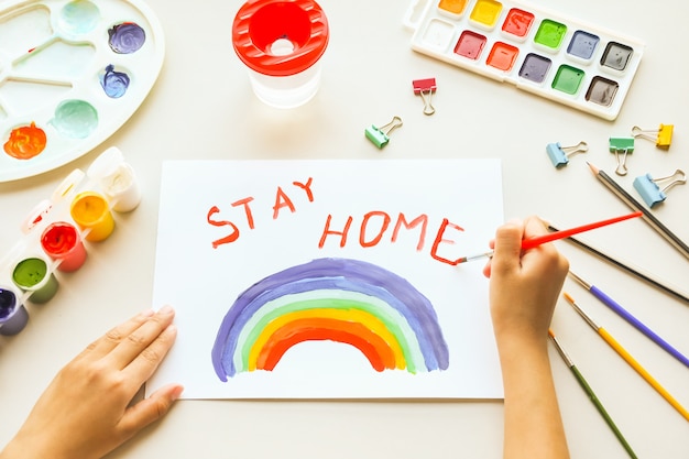 Girl painting rainbow on paper during Covid-19 quarantine at home. Stay home