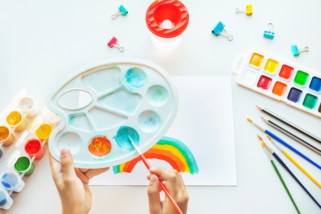 Girl painting rainbow on paper during Covid-19 quarantine at home.