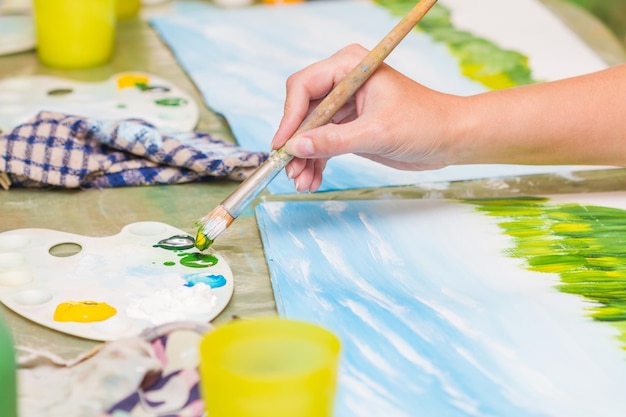 A girl paints a picture by gouache A dirl drawing at white paper The hand and paint brush Closeup selective focus