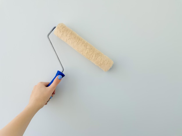 Girl paints the wall with white paint female hand with wall paint roller close up with copy space