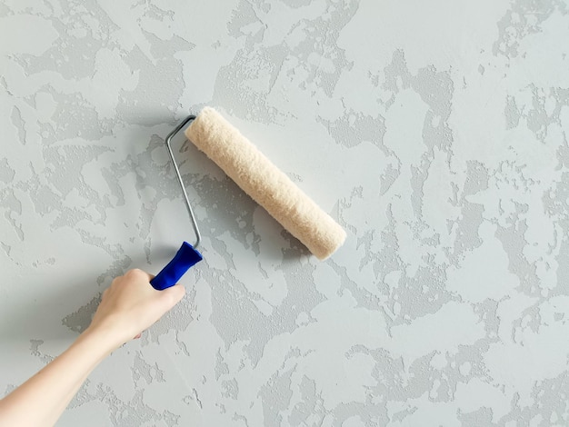 Girl paints the wall with white paint female hand with wall paint roller close up with copy space