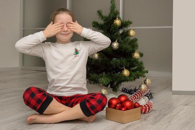 Girl in pajamas closed her eyes sitting by the christmas tree winter holidays