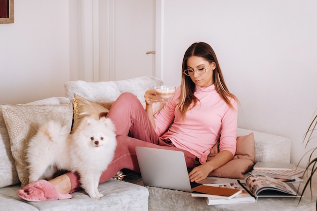 A girl in pajamas at home is working on a laptop with her dog