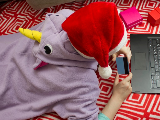 Girl in pajamas and santa hat shopping online with credit card.