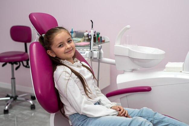 Girl patient shows thumbs up approving pediatric dental service in modern children's clinic Focus on happy smiling positive child Good condition of oral cavity child is sitting in the dental chair