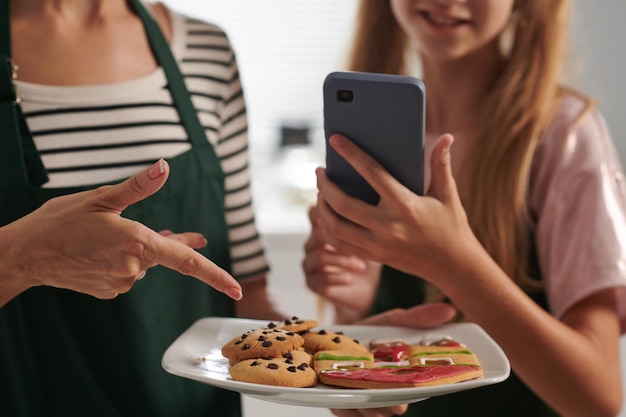 Photo girl photographing plate with cookies she and her mother baked to share post on social media