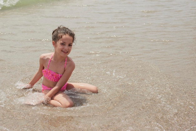 Girl in a pink bikini playing happily on the shore of the beach with the waves on a sunny summer day Vera Spain