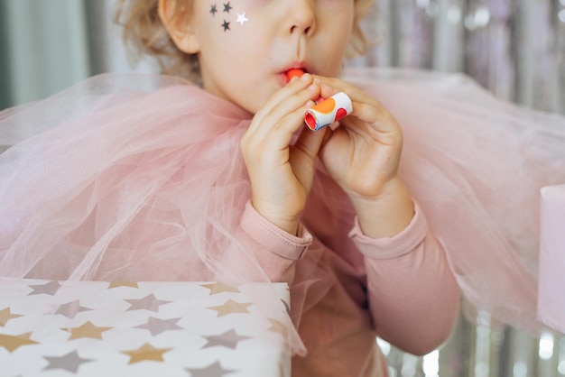 Girl in pink carnival outfit holds festive horn in her hands and is going to blow into it holidays a