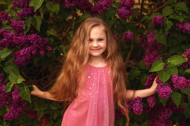 A girl in a pink dress stands in front of purple flowers.