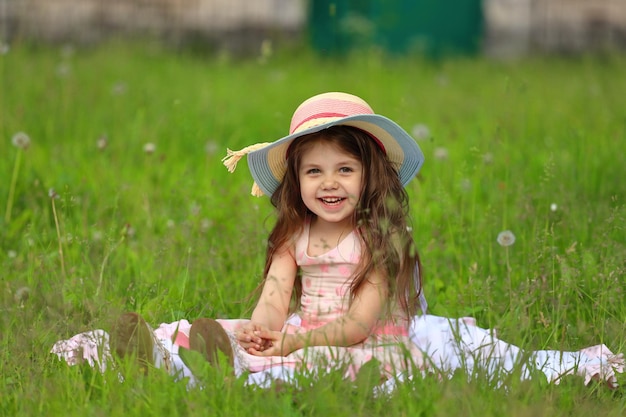 Girl in a pink dress with a hat sits on the grass in the park. High quality photo