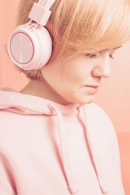 girl in a pink sweatshirt and with pink headphones on a background similar in tone