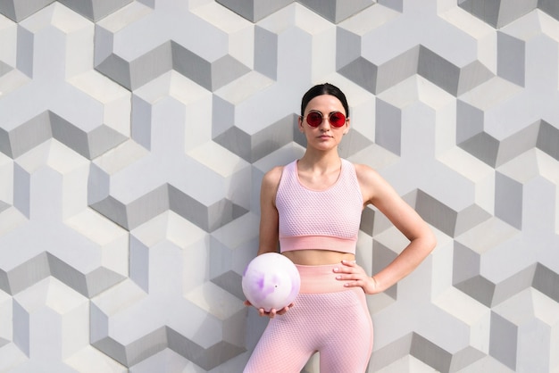 A girl in a pink tracksuit stands with a training ball near the wall