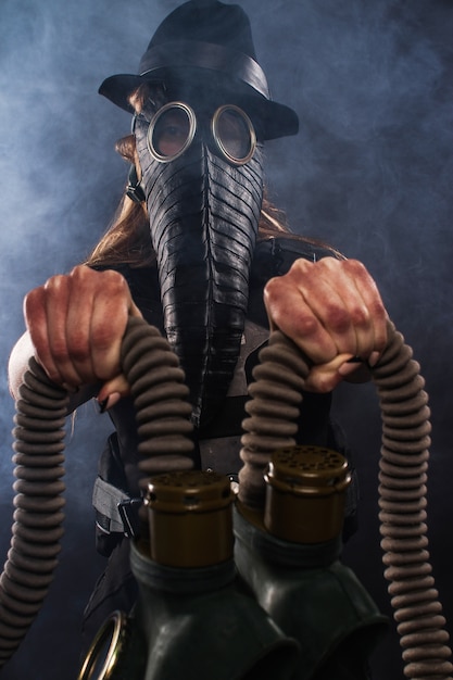 girl in a plague mask holds gas masks in her hands.