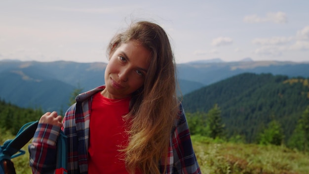 A girl in a plaid shirt stands in front of a mountain with mountains in the background.