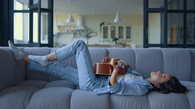 Girl playing guitar in living room Woman lying on couch with musical instrument