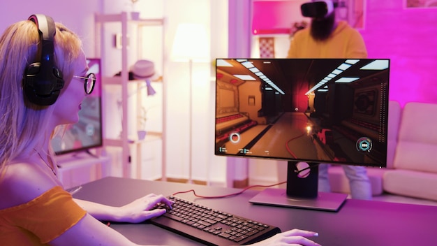 Girl playing shooter games in a room with colorful neon lights. Man with virtual reality headset.