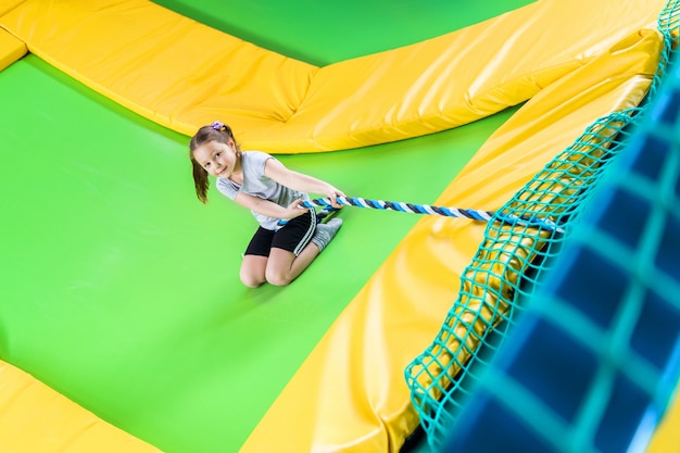 Girl playing in trampoline center jumping and climbing with rope