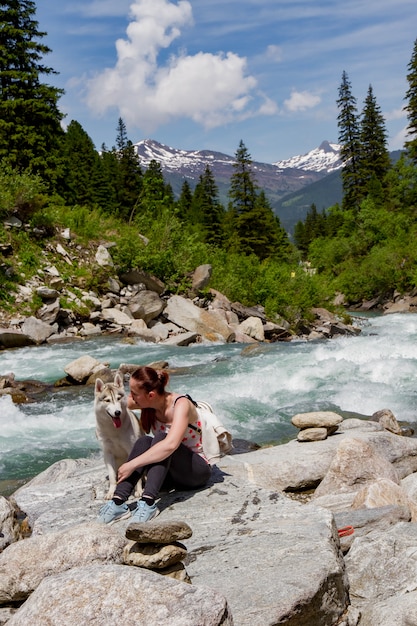 girl playing with a husky dog on the shore of a mountain river