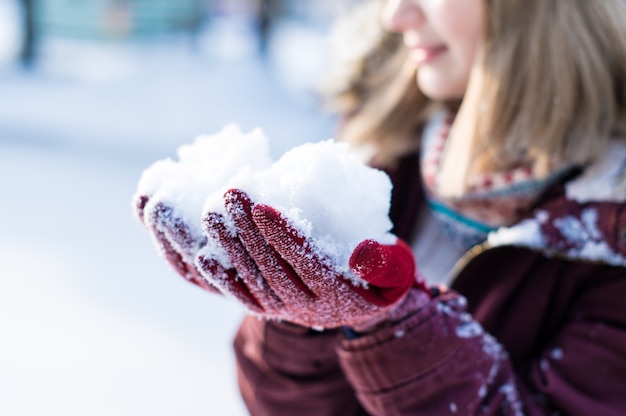 Girl playing with snow in park. Portrait of the happy girl wearing snowy winter clothes