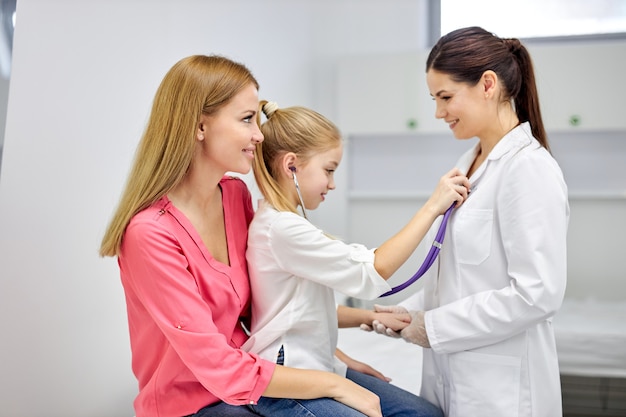 Girl playing with stethoscope in hospital, have fun with doctor woman in medical suit, listen to heartbeat of nurse. medicine, healthcare concept