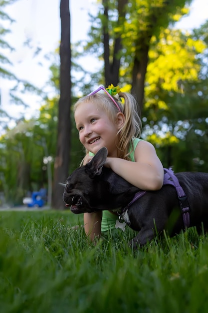 A girl plays in the park with a french bulldog dog hugs him and laughs merrily