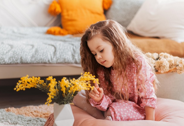 Girl plays with mimosa flowers on the floor in vintage children's bedroom