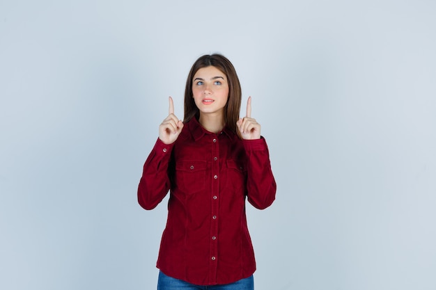 girl pointing up, looking upward in burgundy shirt and looking hopeful.