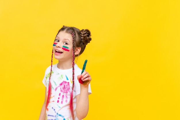 The girl points up A child stained in paint on a yellow isolated background Drawing courses for children Development of children's creativity