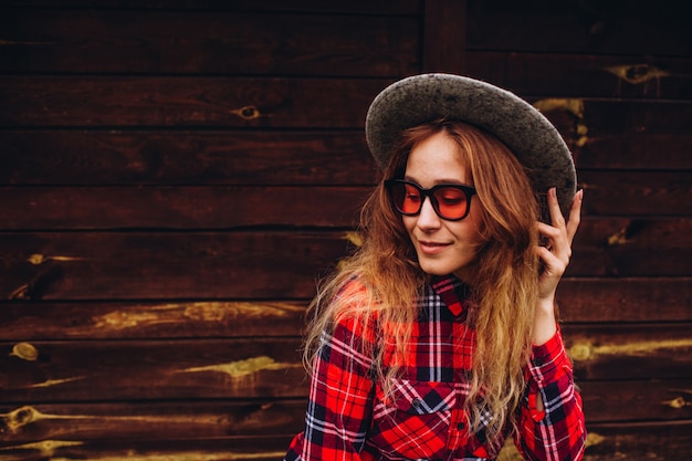 Girl posing against the backdrop of the fence on the old farm, rural life. casual girl, wearing in red and blue plaid shirt, jeans, sunglasses and hat, with brown wooden fence