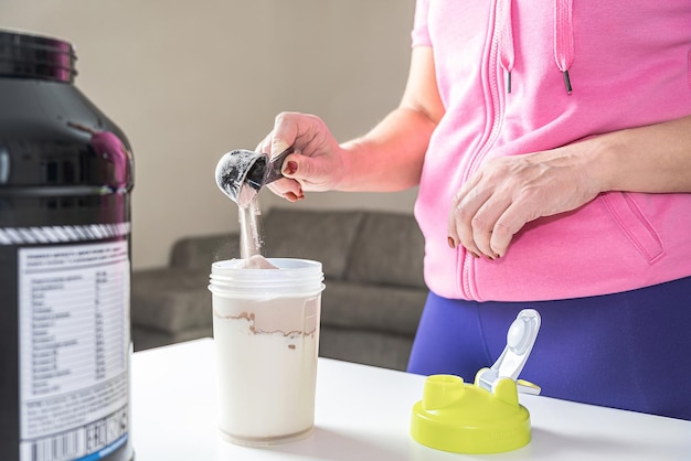 The girl pours sports powder for a cocktail into a shaker with milk. The concept of health and recovery after physical exertion.