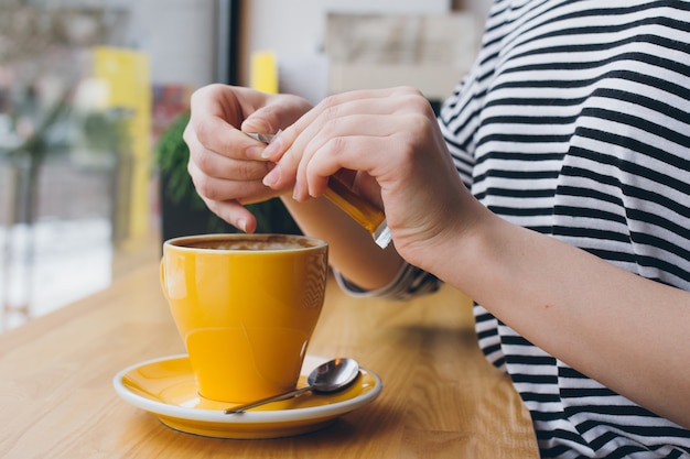 Girl pours sugar from a bag into a mug of coffee