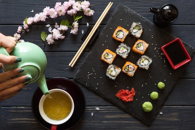 Girl pours tea in a cup with a teapot near Sushi 3