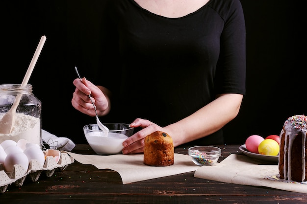 The girl prepares Easter baking, smears the cake with icing and sprinkles with colored powder