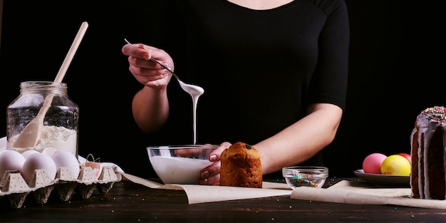 The girl prepares Easter baking, smears the cake with icing and sprinkles with colored powder