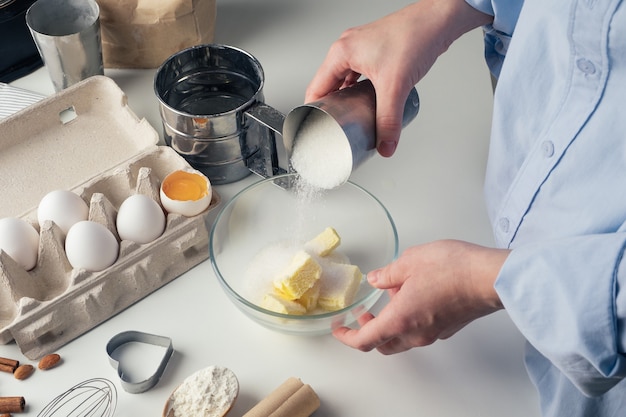 Girl preparing cookies in the kitchen, pouring sugar, close-up.