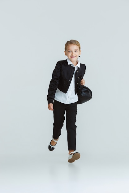 Girl preparing for school after a long summer break. Back to school. Little female caucasian model posing in school's uniform on white  wall. Childhood, education, holidays concept.