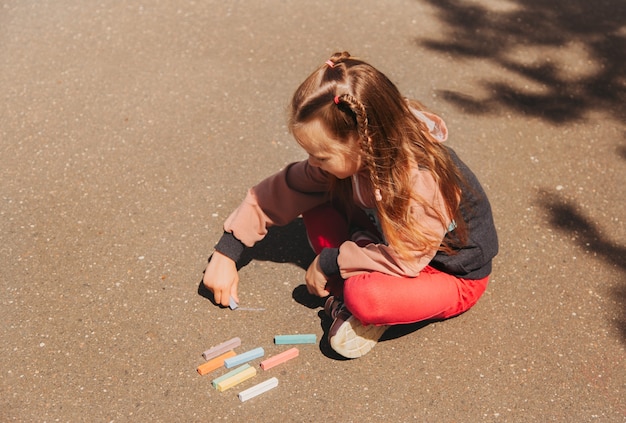 Girl preschooler draws with chalk on the asphalt in summer in the park