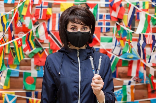 A girl in a protective black mask and syringes in her hand calls for vaccination during a pandemic.