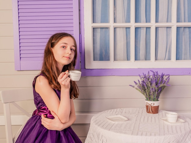 A girl in a purple dress drinks tea while sitting at the table A teenager at home