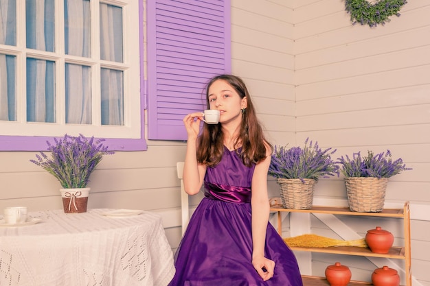 A girl in a purple dress drinks tea while sitting at the table A teenager at home