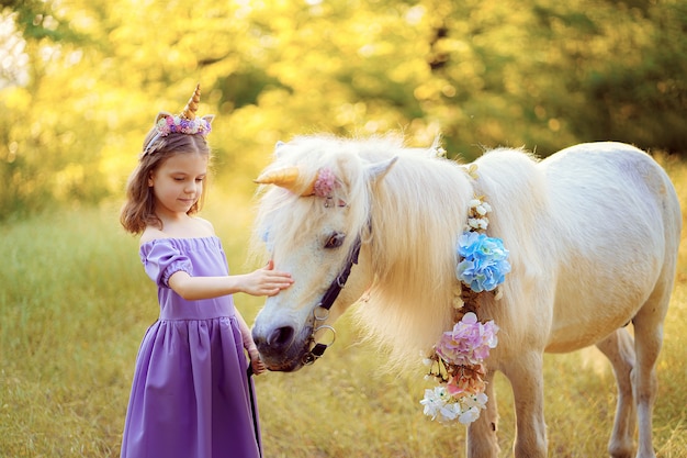 Girl in purple dress with wreath of a unicorn in hair hugging white unicorn