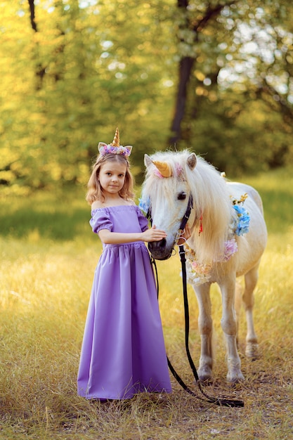 Girl in purple dress with wreath of a unicorn in hair hugging white unicorn