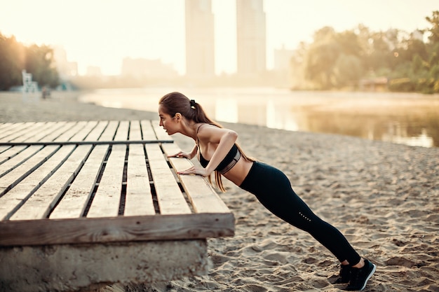 Girl do push ups on wooden platform on river beach