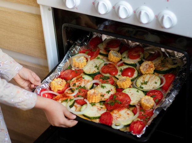 the girl puts a baking tray with vegetables in the oven